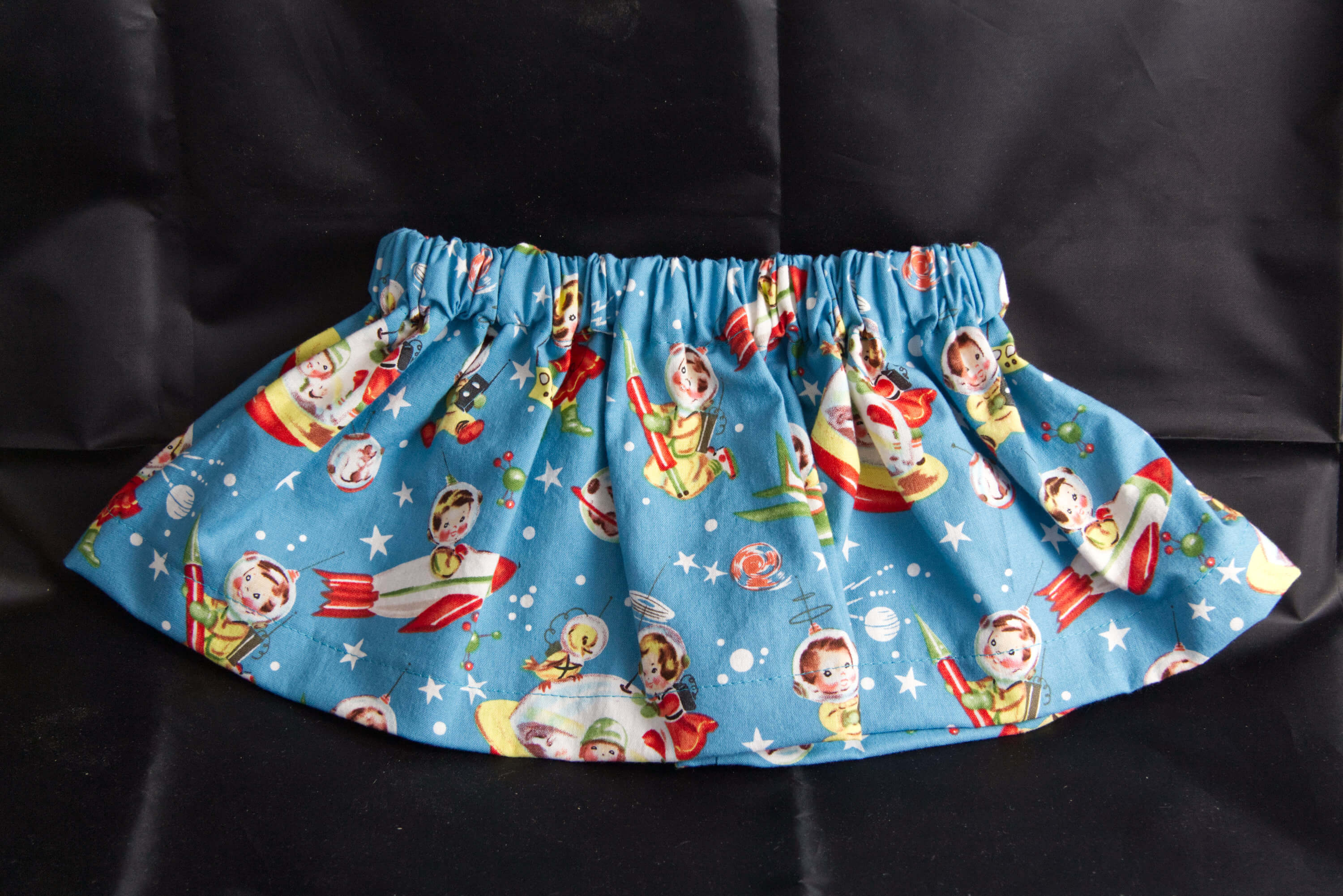 A sky blue skirt that has depictions of childern in space suites.  Flying rocket ships and space walking.